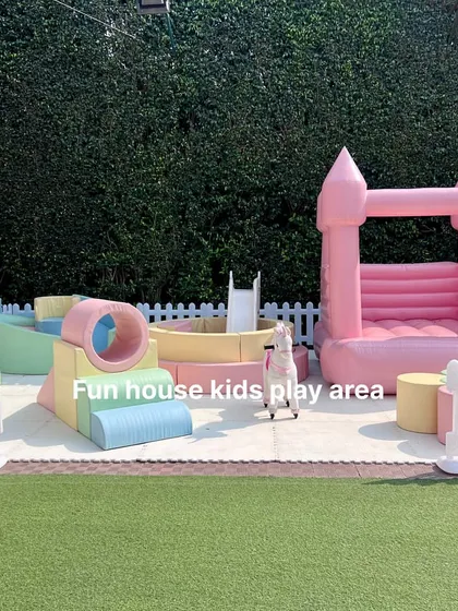 A complete pastel-themed soft play area set up outdoors, featuring a pink bounce castle, a ball pit, and various soft play elements for climbing and exploring.