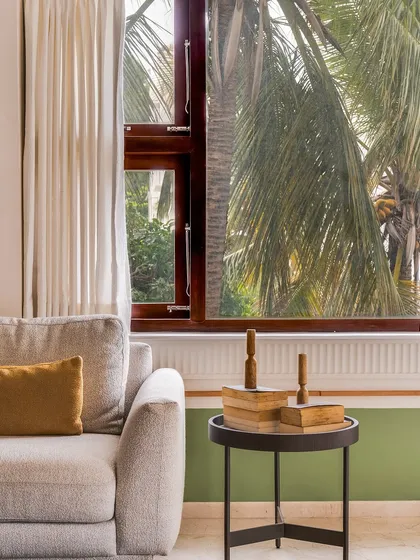 In this living room, the goal was openness. The large window brings the lush outdoors in, and the color palette of light wood and soft greens creates a serene atmosphere. A simple side table with books and decor adds a personal touch.