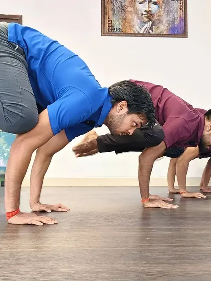 A group of students practice a variation of crow pose in unison, demonstrating collective strength and focus.