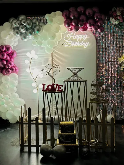 A low-light view of the magenta and silver birthday decor. The ambient lighting and neon sign create a more intimate and cozy atmosphere, perfect for evening celebrations in Hubli.