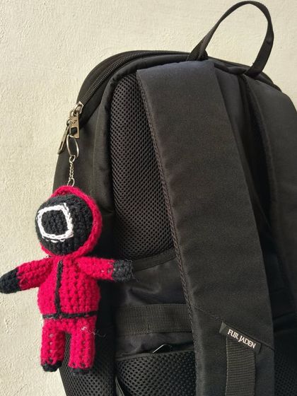 Showing how the Squid Game amigurumi can be used as a cool keychain or bag charm on a backpack.