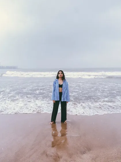A wide shot emphasizing the solitude of the model against the vastness of the ocean. The reflection on the sand adds a beautiful symmetry.