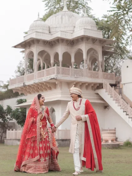 A classic fairytale moment comes to life. The bride in her magnificent red lehenga and the groom in his regal sherwani walk hand in hand against the stunning architecture of a palace. This is the essence of a royal Indian wedding.