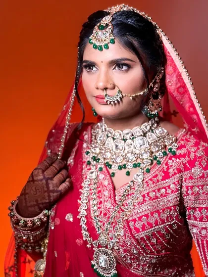 A stunning portrait of a dusky bride in a traditional red lehenga. The makeup is designed to complement her skin tone, with a focus on her eyes and a well-defined look.