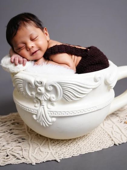 A creative newborn portrait with the baby posed as if sleeping inside a large teacup prop. A whimsical and adorable concept.