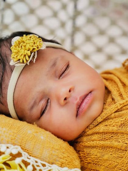 A close-up of a sleeping baby in a yellow wrap. The soft texture of the wrap and the delicate headband add beautiful details to this peaceful portrait.