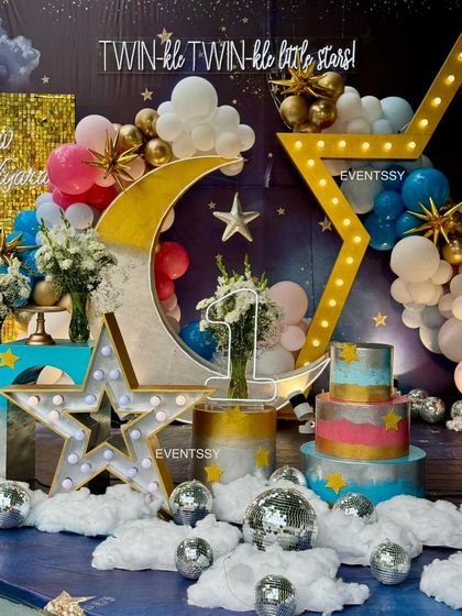 A close-up of the cake and dessert area, featuring a lit-up star, a crescent moon prop, and a colorful tiered cake. The small disco balls scattered on the "clouds" add a fun, sparkling touch.