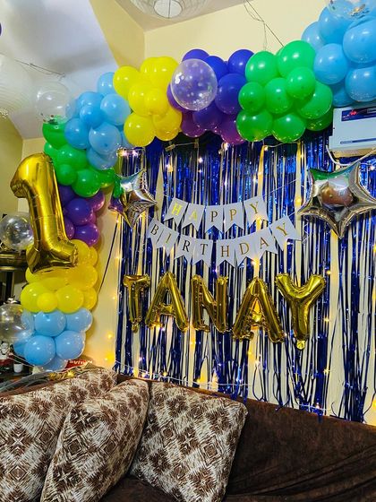 This image shows the complete setup for Tanay's first birthday, including the large '1' foil balloon, the name in gold letters, and the 'Happy Birthday' banner.