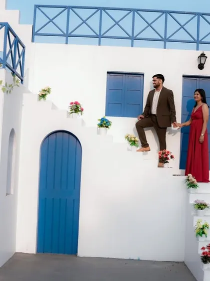 A fairytale moment on the steps of a beautiful Santorini-style building. The groom helps his bride-to-be, dressed in a flowing red gown, creating a classic and romantic cinematic shot.