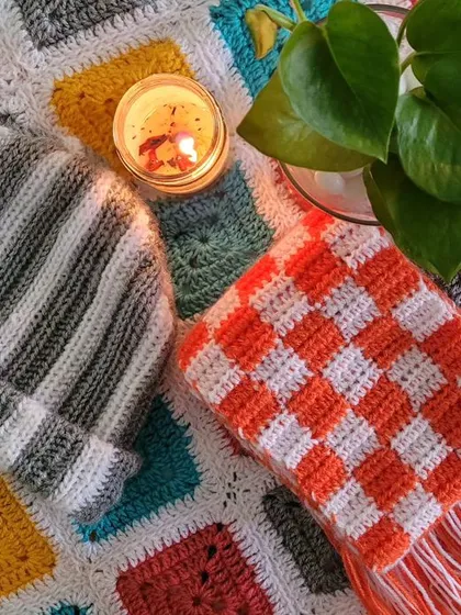 Stripes and checks are always in style! This picture shows a striped beanie and a checkered scarf I made, resting on a colorful granny square blanket. These are the kinds of fun patterns I'm working on for my winter collection.