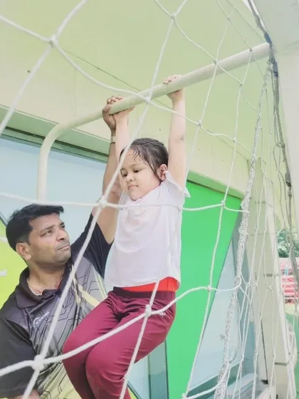 A young student builds upper body strength on the monkey bars during a gymnastics session at our Summer Fungama, guided by an attentive instructor. We focus on developing foundational motor skills in a safe and encouraging setting.