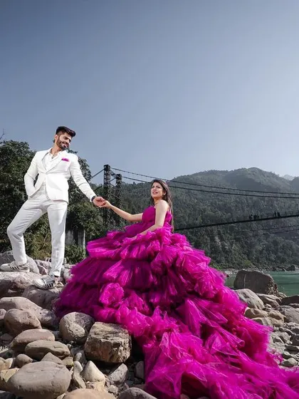 A breathtaking wide shot in Rishikesh, with the bride's vibrant gown flowing over the riverside rocks. This image is a perfect example of how I combine fashion, drama, and nature to create a truly epic pre-wedding photograph.