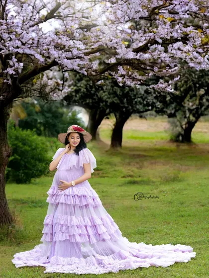 A serene solo portrait in a lavender ruffled gown and hat, set against a backdrop of blooming trees.