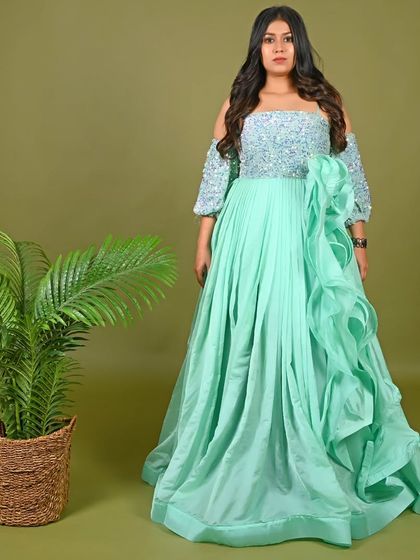 Our mint green off-the-shoulder gown is a fresh and modern choice for any celebration. It features a sequined bodice and a cascading side ruffle for added flair.