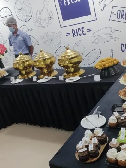 A dessert and snack counter at a corporate event. The spread includes a variety of cupcakes, Indian sweets like ladoo, and other baked goods.