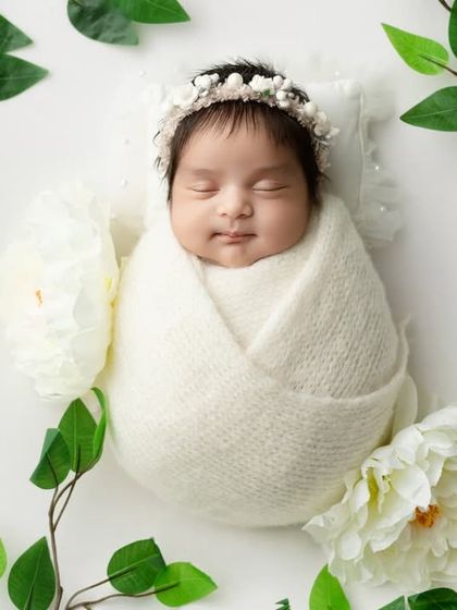 A simple and elegant setup with a baby in a white swaddle, framed by green leaves and white flowers.