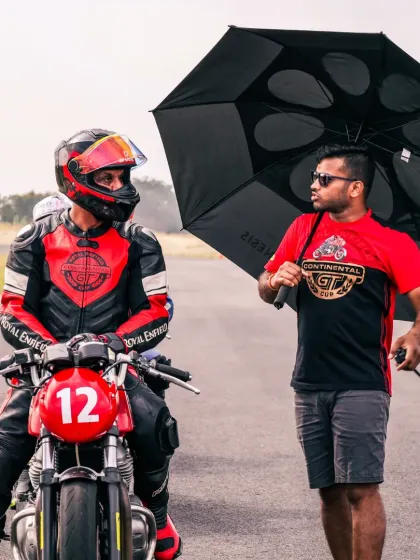 A coach holding an umbrella for a rider, showcasing our commitment to supporting our students in every way, on and off the track.