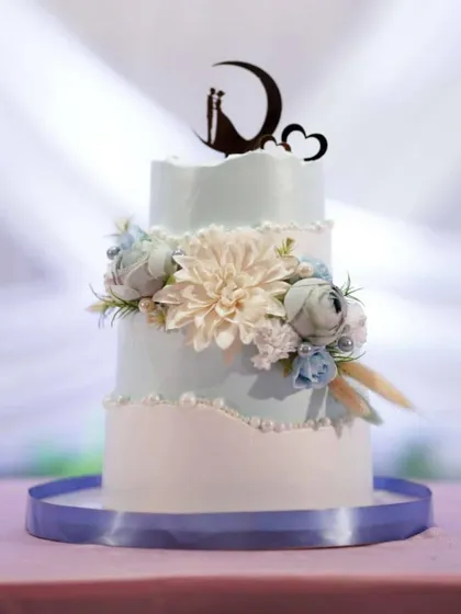 This two-tier engagement cake was crafted to perfectly match the couple's outfits and the event's decor. The soft blue and white tones, combined with a large dahlia and a moon topper, create a dreamy, celestial vibe.