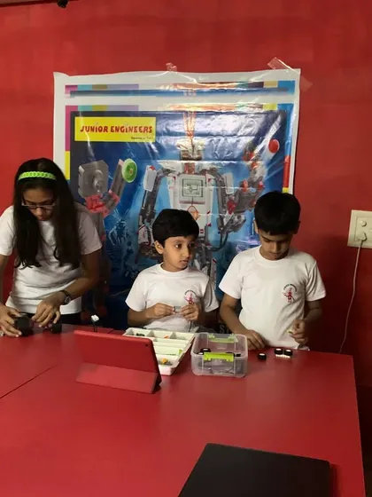 A group of students works collaboratively at a table, sorting through parts and building their robotics projects.