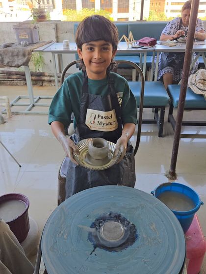 Success. Holding up his first wheel-thrown pot, this little artist is all smiles. Every child takes home what they make, a tangible reminder of their creative achievement.