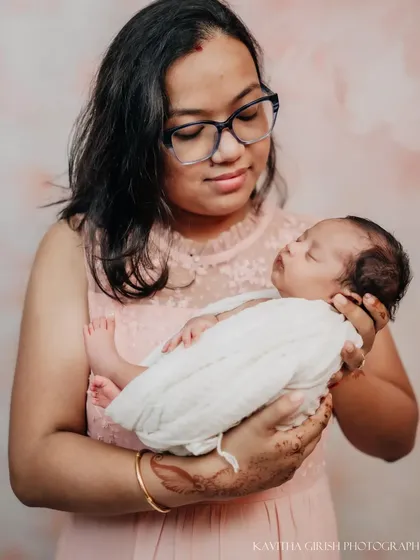 A mother cradling her precious newborn. The soft pink backdrop and simple styling keep the focus entirely on the love and tenderness of the moment.