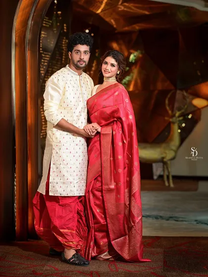 A full-length portrait of actors Sauraseni Maitra and Soumya Mukherjee for Sangbad Pratidin. Their coordinated red and white traditional outfits create a visually harmonious and elegant couple's portrait.