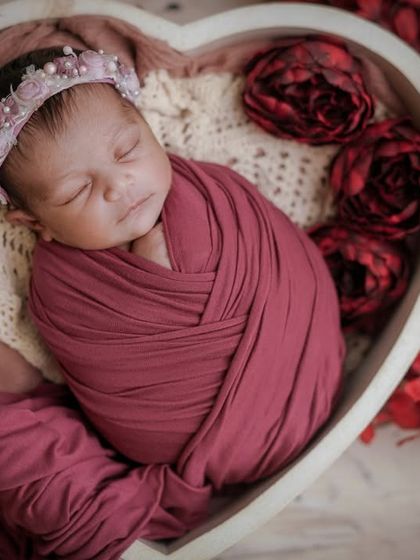 Every cuddle, a moment to treasure. This baby, swaddled in a heart bowl, is surrounded by soft fabrics and flowers, creating a romantic scene.