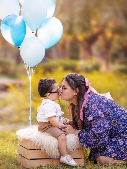 An adorable outdoor moment between mother and son during his first birthday photoshoot. The balloons and natural setting add to the celebratory feel.