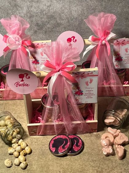 Our customisable return gift favours are perfect for a baby shower. This image shows our "Barbie" themed pinewood baskets filled with pink foot-shaped chocolates and flavoured foxnuts.