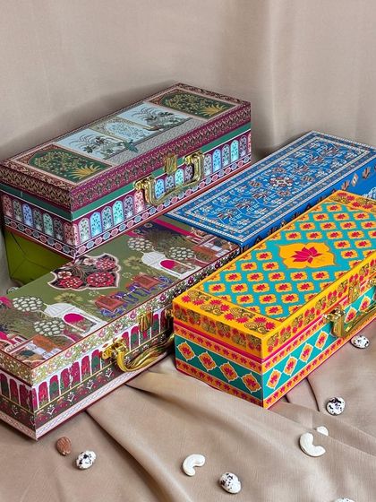 This image displays a variety of my rectangular designer trunk boxes. Each box has a unique color palette and pattern, from floral and geometric to traditional motifs, offering a wide range of choices for your festive gifts.