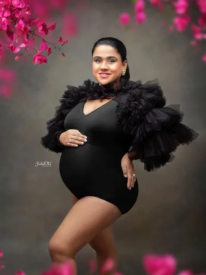 This mama is absolutely glowing in a bold black bodysuit with dramatic ruffled sleeves. Paired with a floral frame, it creates a modern and high-fashion maternity look.