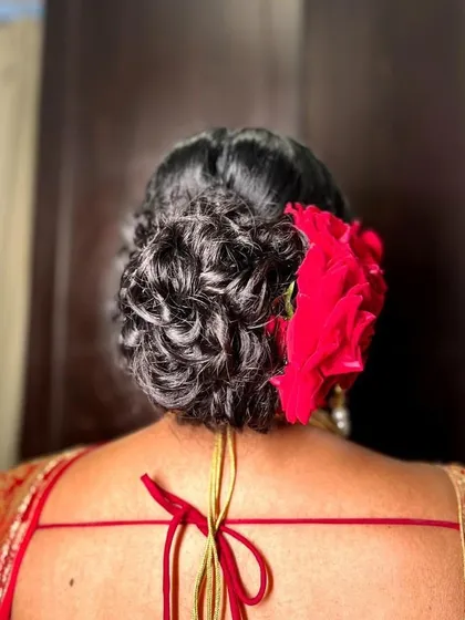 A beautiful messy bun with silver-toned natural hair, adorned with a large red rose. This shows that you can have a stunning bridal style at any age.