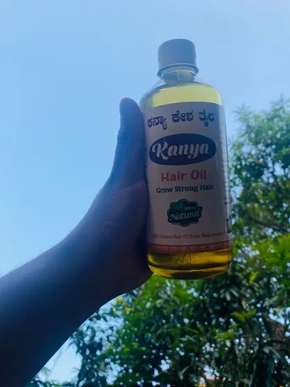 Holding up a bottle of my golden-hued Kanya Hair Oil against the sky. The color comes from the rich blend of over 40 natural herbs infused in coconut oil.