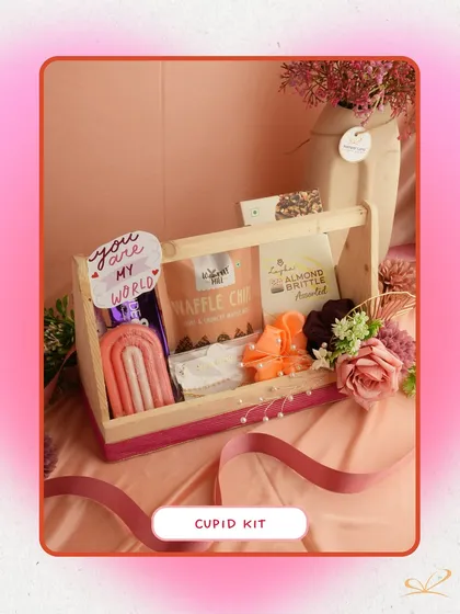 The 'Cupid Kit' is a charming wooden crate filled with a rainbow candle, waffle chips, and other sweet treats. The "You are my world" tag adds a personal touch to this delightful assortment.
