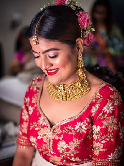 A beautiful close-up of a South Indian bride, highlighting her floral hair accessory, traditional gold jewelry, and happy smile.