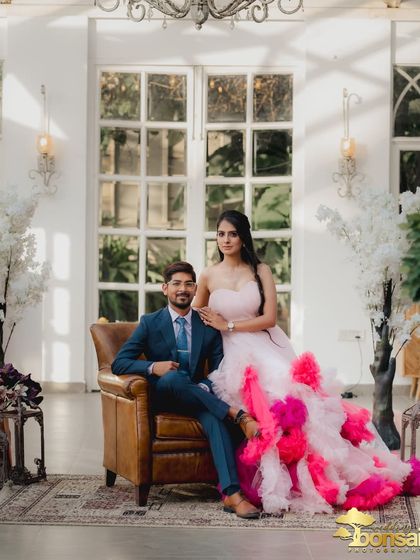 A classic, regal portrait of the couple. The groom is seated, and the bride stands beside him, creating a powerful and elegant composition.