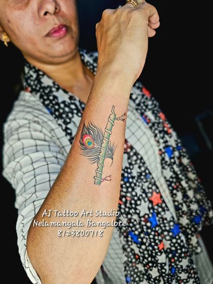 A colorful tattoo of a peacock feather wrapped around a bamboo flute.