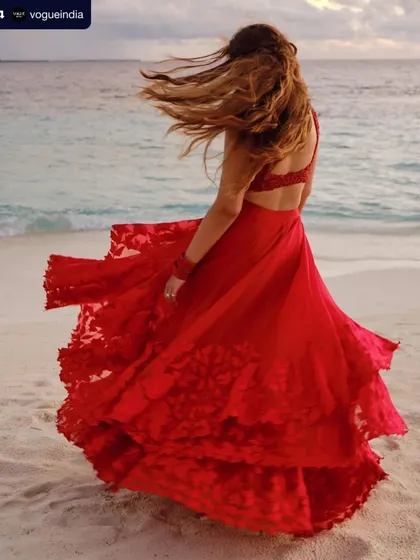 A magical moment from a beach wedding, featured in Vogue. The bride's red gown flows in the wind, a perfect picture of romance and freedom.
