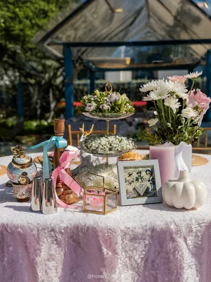 An elegantly styled table centerpiece with a tiered stand, vintage photo frames, and pastel-colored candles and props, embodying the Victorian tea-party theme.