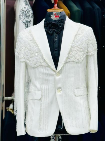 A full view of the white tuxedo with fringe detailing. The dramatic sleeves and unique silhouette make this a one-of-a-kind couture piece.