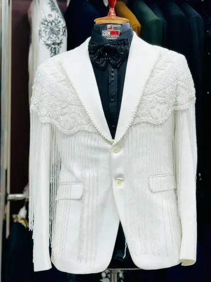 A full view of the white tuxedo with fringe detailing. The dramatic sleeves and unique silhouette make this a one-of-a-kind couture piece.