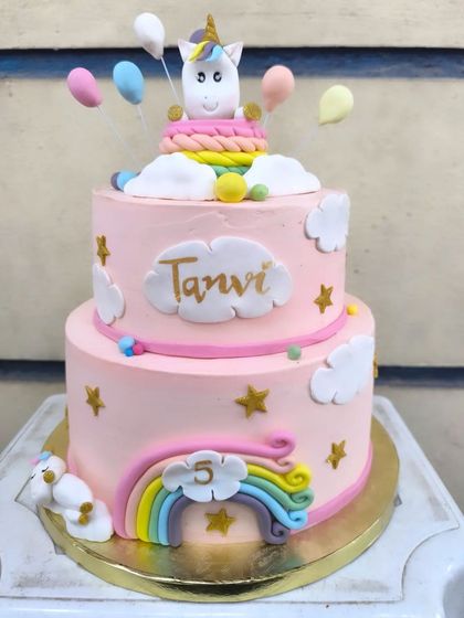 A close-up of the magical unicorn birthday cake. The details include a fondant unicorn topper, pastel balloons, and fluffy clouds on a soft pink buttercream base.