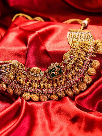 An antique gold necklace, rich with intricate details. This piece showcases traditional craftsmanship with meenakari, gold coins, and ruby accents, designed to add elegance to any outfit.