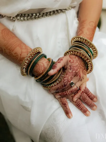 A close-up of the bride's hands, adorned with intricate henna and beautiful green and gold bangles. A perfect shot of traditional bridal details.