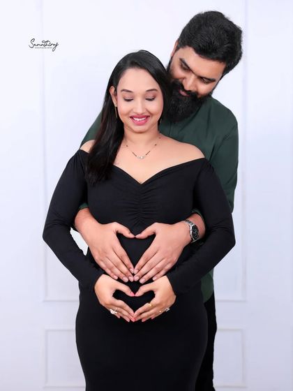 A loving couple portrait with their hands forming a heart on the baby bump. The simple black outfits and clean background keep the focus on this beautiful symbol of love.