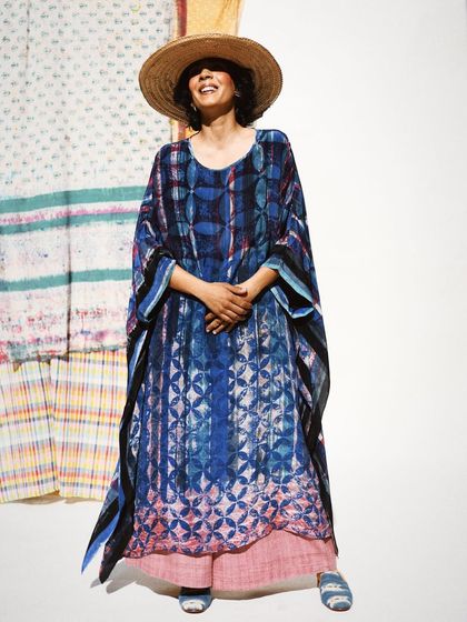 A joyful, full-length portrait for Wandering Silk. The model's smile and the flowing silhouette of the kaftan against a backdrop of printed textiles perfectly capture the brand's free-spirited and artistic vibe.