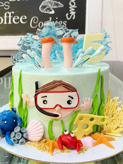 An underwater adventure cake for a 5th birthday. The design shows a snorkeler exploring the sea, complete with a crab, octopus, and coral.