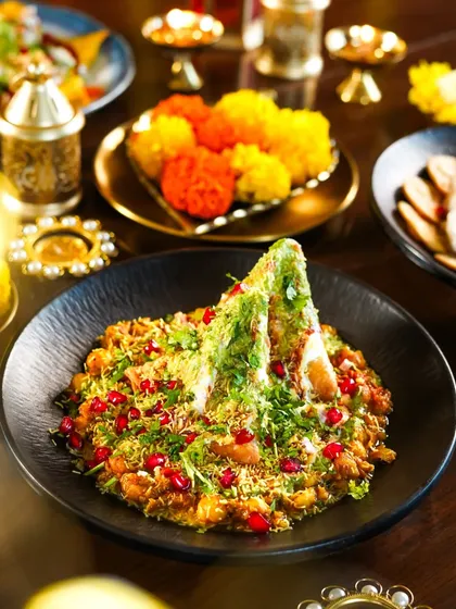 A modern take on Samosa Chaat, deconstructed and topped with pomegranate seeds and sev. The festive styling with marigold flowers and diyas elevates this classic street food dish.