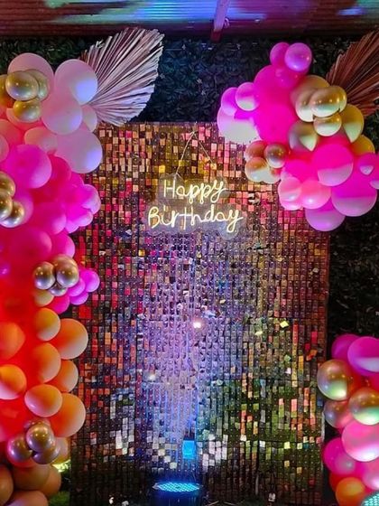 A vibrant photo backdrop with a multi-colored sequin wall, a neon sign, and a beautiful garland of pink and orange balloons.