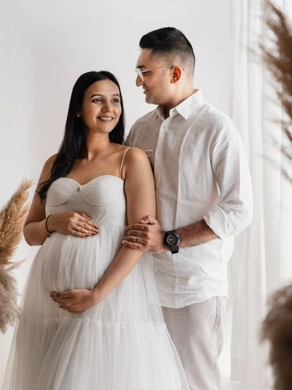 A classic couple's pose that always looks so beautiful. They are both looking at each other with so much love, with their hands cradling the baby bump. The all-white theme feels so fresh and pure.